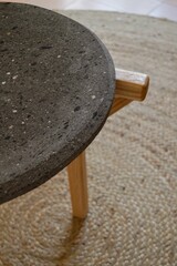 Small side table from a natural stone top, and wooden legs on a round jute rug, close-up shot