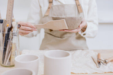 woman ceramist in the workshop makes mugs out of clay. a small business or hobby is the creation of ceramic products. an oriental young woman ceramist makes dishes and vases out of clay. handmade
