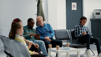 African american man and senior patient waiting together at hospital reception, looking at online...