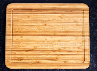 Top view of a rectangular wooden chopping board on the dark-colored surface
