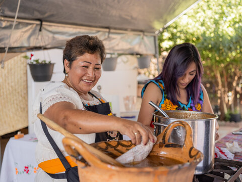 Indigenous woman and her daughter putting turkey legs in the mole