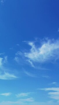 Vertical footage of white puffy clouds floating in the blue sky in summer in daylight