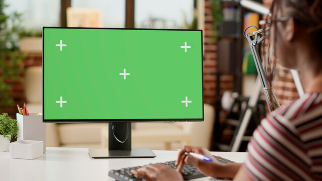 Businesswoman working remotely with greenscreen on computer, using chroma key template at home. Doing remote work with isolated mockup display, blank background and copyspace on monitor.
