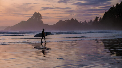 Tofino Vancouver Island Pacific rim coast, surfers with surfboard during sunset at the beach,...