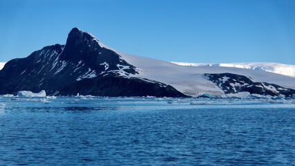 Fototapeta na wymiar Icebergs floating at the base of snow covered mountains in Cierva Cove, Antarctica