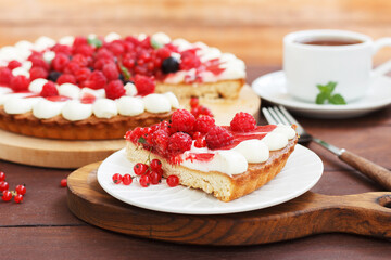 A piece of berry pie with cheese cream on a plate on a wooden background with a cup of tea.