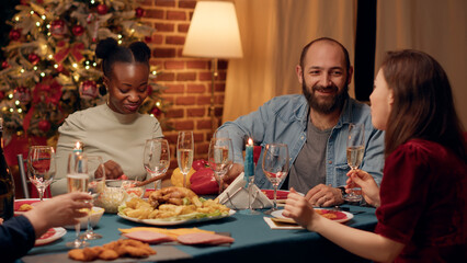 Cheerful multiethnic family members toasting champagne while enjoying Christmas dinner at home. Festive happy people clinking sparkling wine glasses while celebrating winter holiday.