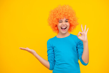 Birthday kids party. Funny kid in curly clown wig isolated on yellow background. Excited teenager, glad amazed and overjoyed emotions.