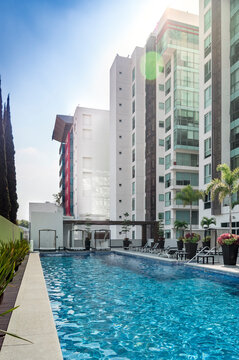 complex of luxury buildings, with pool amenity, lounge chairs, planters with palm trees, rest areas at the back