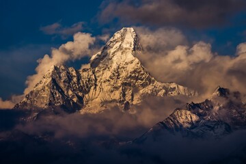 Peak of Ama Dablam mountain in clouds and fog with snow reflecting sunlight