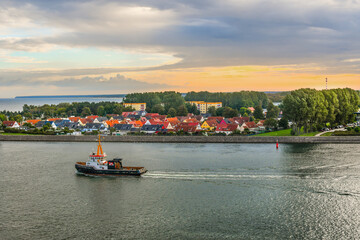 Naklejka premium A tugboat sails past luxury waterside homes in the Baltic Sea off of the coast of Copenhagen Denmark at sunset.