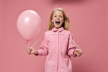 Obraz na płótnie Canvas a beautiful, happy girl in a pink shirt stands on a pink background and smiling broadly at the camera holds a pink balloon in her hand
