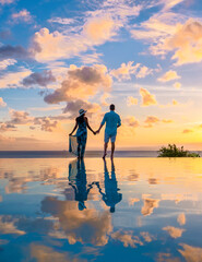 Young men and women watching the sunset with reflection in the infinity swimming pool at Saint...