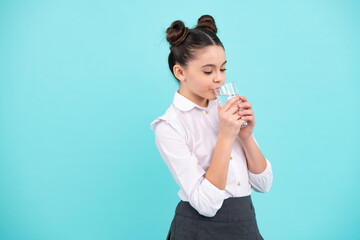 Teenage girl drinking water from glass on blue background. Daily life health. Drink water for health care and body balance. Thirsty child, dehydration.