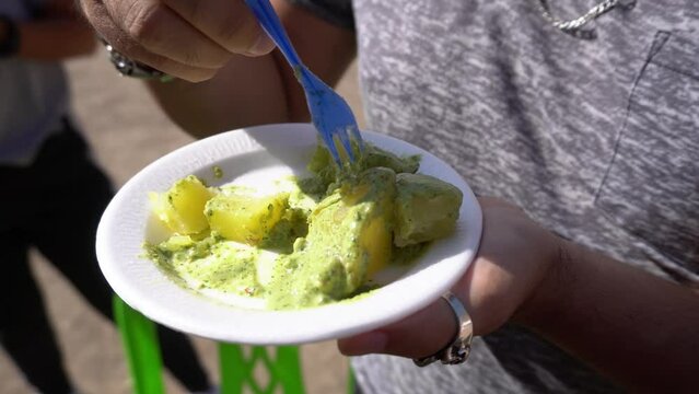 Closeup of human hands holding wite plate tasting pesto potatoes