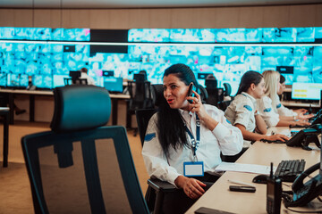 Female security guard operator talking on the phone while working at workstation with multiple...