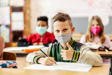 A pupil writes down schoolwork and shows thumbs up during covid 19.