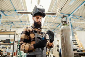 A heavy industry worker adjusting welder and preparing to weld metal parts in facility.