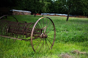 Large wheeled rusty horse rake on green grass