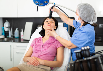 Experienced cosmetologist working in the clinic makes a young woman client a vacuum cleaning of the face with the help ..of the device