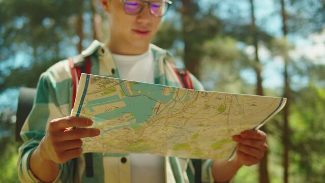 Asian man tourist walking in forest camp. Young hiker traveling and hiking alone, guy using map and wearing backpack. Summer tourism, wild nature.