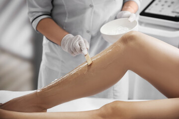 Fototapeta premium Professional cosmetologist applying gel on client's leg before laser epilation procedure in salon, closeup