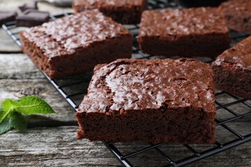 Cooling rack with delicious chocolate brownies and fresh mint on wooden table, closeup