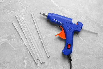 Blue glue gun and sticks on light grey marble table, flat lay
