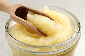 Body scrub with scoop in glass jar on light grey background, closeup