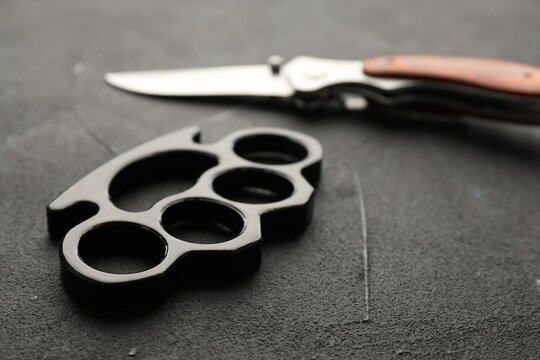 Brass knuckles and knife on black stone background, closeup