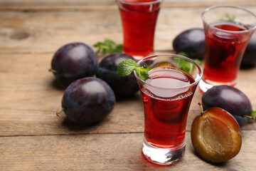 Delicious plum liquor, mint and ripe fruits on wooden table. Homemade strong alcoholic beverage