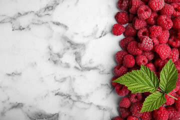 Fresh ripe raspberries with green leaves on white marble table, flat lay. Space for text