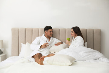 Fototapeta premium Happy couple in bathrobes resting on bed at home