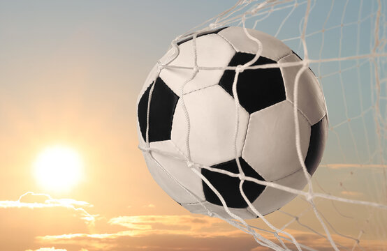 Soccer ball in net against sky at sunset