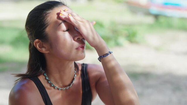 4K Attractive Asian woman in swimwear applying sunblock lotion on her face while sitting on tropical beach in sunny day. Wellness female enjoy outdoor lifestyle at the sea on summer holiday vacation