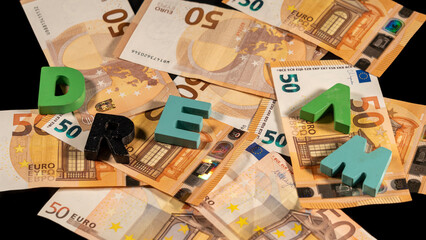Message "dream" in colorful wooden letters, on a pile of fifty euro notes. European currency.