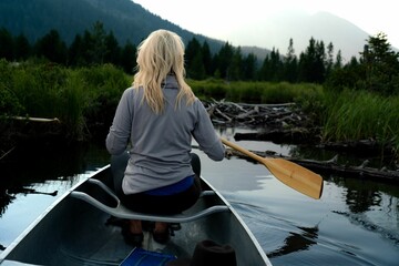 Rear view of a blonde woman canoeing on a peaceful mountain lake