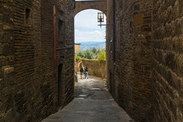 Couple walking in an medieval allwy with stone wall at San Gemignano, Tuscany, Italy.