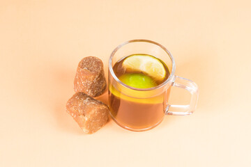 agua de panela with lemon and cubes or sugar cane candy and lemon on a orange background with copy space, typical food from Colombia