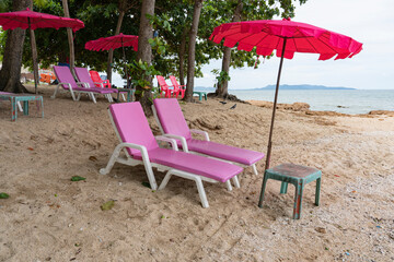 Two sun loungers with a red parasol stand on the seashore.