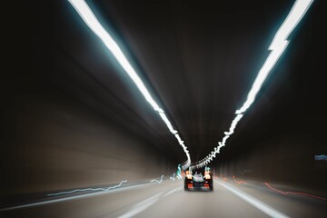 Blurred shot of a car driving fast in a dark tunnel with lights on the ceiling