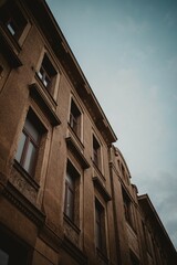 Vertical low-angle shot of a brown building with windows and a background of blue sky