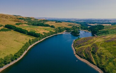 Beautiful shot of the Glencorse Reservoir surrounded by green trees and land