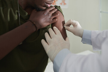 Military doctor using cotton swab moistened with alcohol to wipe arm of soldier before vaccination