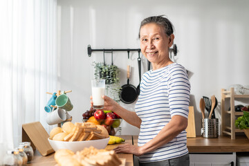Asian senior mature woman drinking a glass of milk in kitchen at home. 