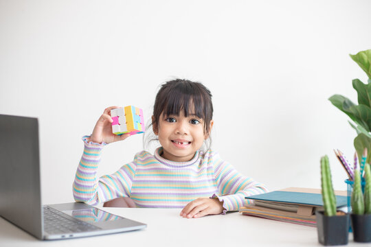 NAKHON RATCHASIMA, THAILAND - JULY 14, 2022:Asian little cute girl holding Rubik's cube in her hands. Rubik's cube is a game that increases the intelligence of children.