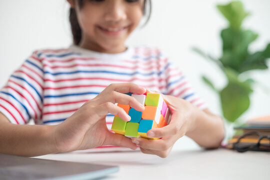 NAKHON RATCHASIMA, THAILAND - JULY 14, 2022:Asian little cute girl holding Rubik's cube in her hands. Rubik's cube is a game that increases the intelligence of children.