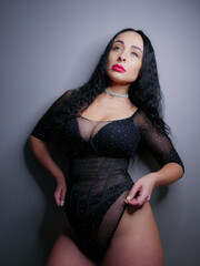 Fototapeta premium brunette with red lipstick on her lips in a black bodysuit on a gray background