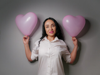 brunette with pink lipstick on her lips with pink balloons in the form of hearts on a gray background