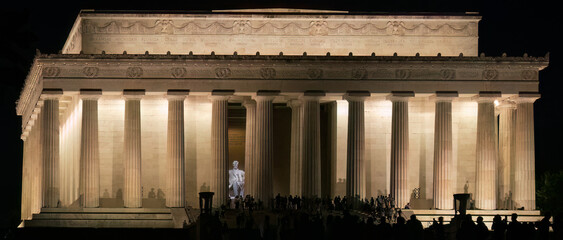 Lincoln Memorial at night lit up with people in front of it, Abraham Lincon's statue clearly visible